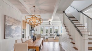 Un comedor amplio con una mesa y sillas de madera, una lámpara colgante y una escalera con barandillas blancas.