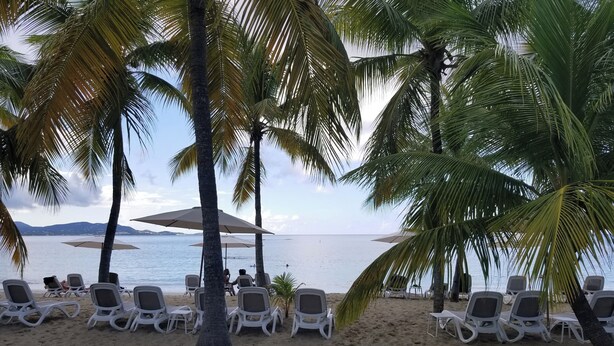 Une plage avec des chaises longues blanches et des parasols.