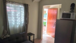 Un salon avec un canapé, une petite table, un four à micro-ondes et une porte donnant sur l’extérieur.