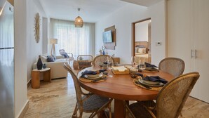 Een eetgedeelte met een ronde houten tafel voor vier personen, omringd door rieten stoelen. Een televisie is aan de muur boven de tafel bevestigd.