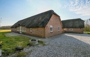 A brick building with a thatched roof, a gravel driveway, and a grassy area with a planter. - Nice home in Ulfborg with sauna (Ulfborg)