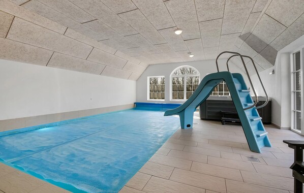 An indoor swimming pool with a slide, tiled walls, and large windows. - Nice home in Ulfborg with sauna (Ulfborg)