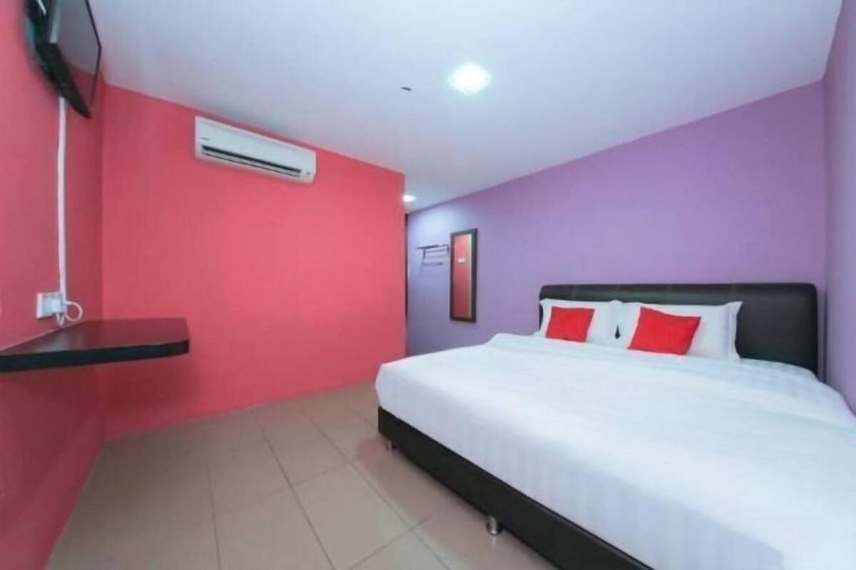 A hotel room with a bed, a red wall, a white ceiling, and an air conditioning unit.