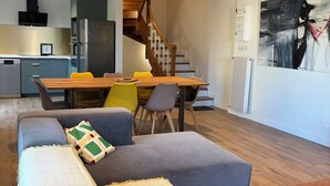 A modern living room with a sofa, a dining table with chairs, a kitchen area, and a staircase. - Country house in the heart of the Parc des Volcan, 10 minutes from Clermont-Ferrand (Romagnat)
