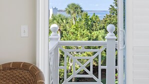 Un balcon doté d’une balustrade blanche, d’une chaise en osier et offrant une vue sur un paysage côtier avec des arbres et l’océan.