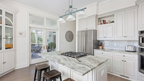 A modern kitchen with white cabinetry, a marble island, stainless steel appliances, and a dining area with a glass door leading outside.