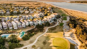 Vue aérienne d’une zone résidentielle côtière, avec des maisons, un terrain de golf et une plage.