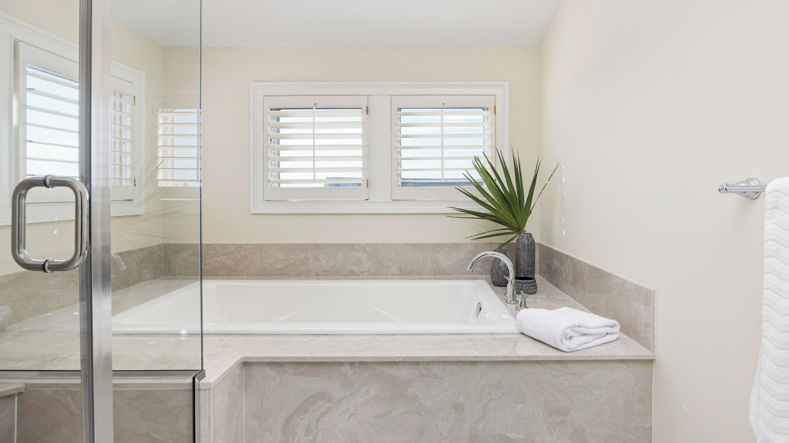 A bathroom with a glass-enclosed shower, a bathtub, and a window with blinds.