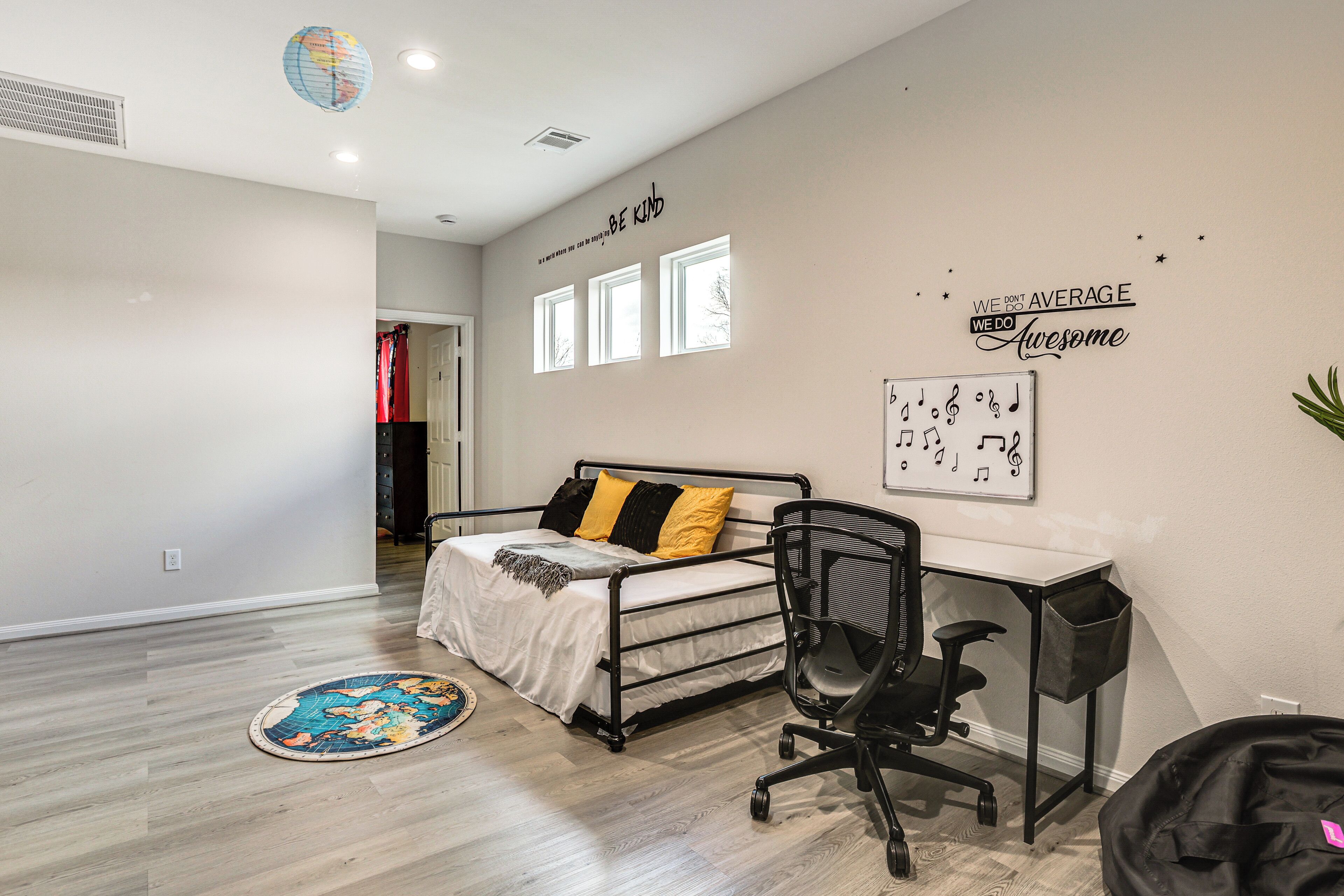 A bedroom with a bed, a desk, and a chair. There are three windows and a globe on the ceiling.