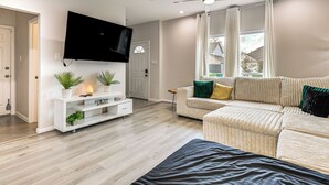 Een moderne woonkamer met een flatscreen-tv, een wit tv-meubel, een beige bank en een plafondventilator.