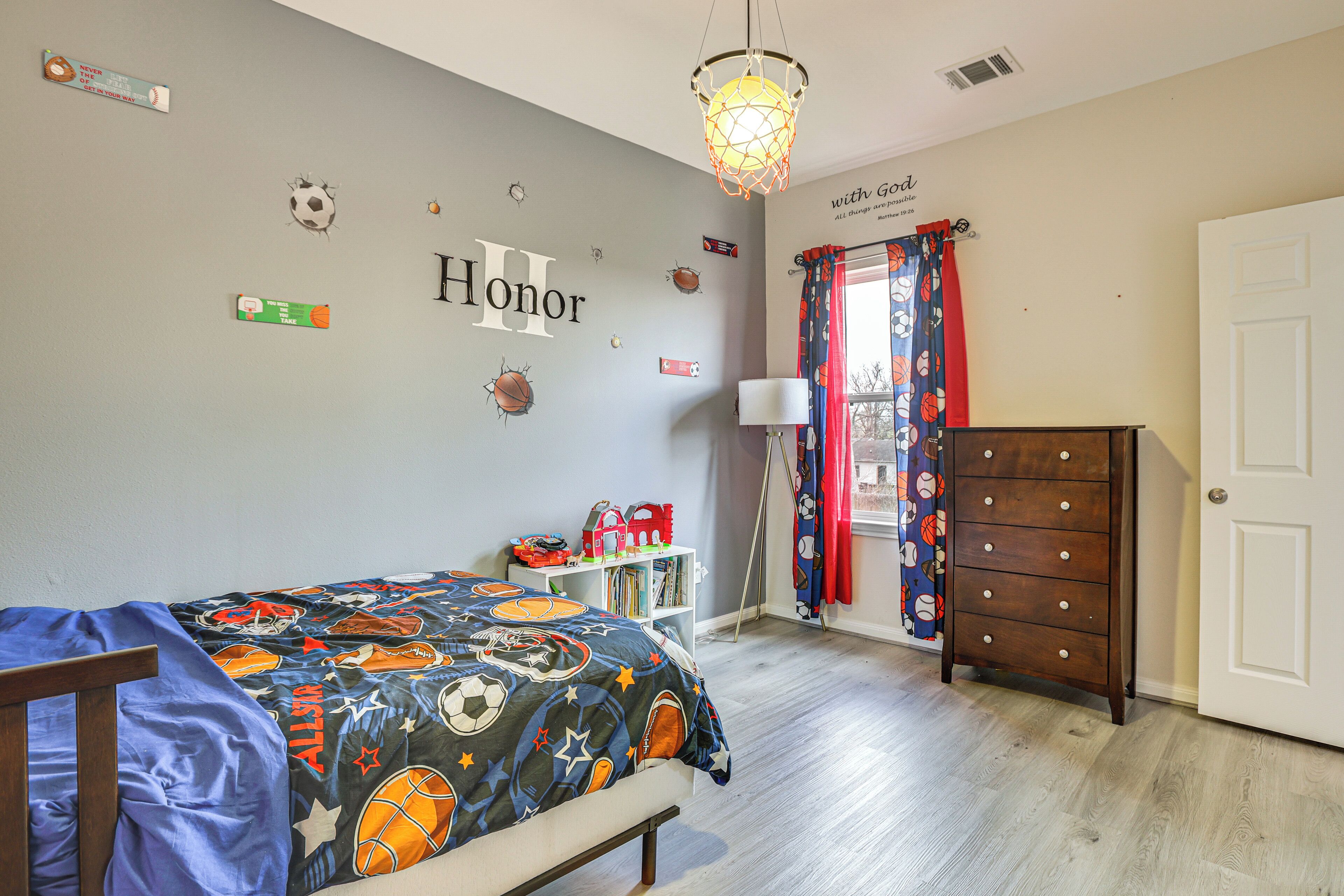 Une chambre avec un lit, une commode, une étagère remplie de livres et un mur décoré sur le thème du basketball.