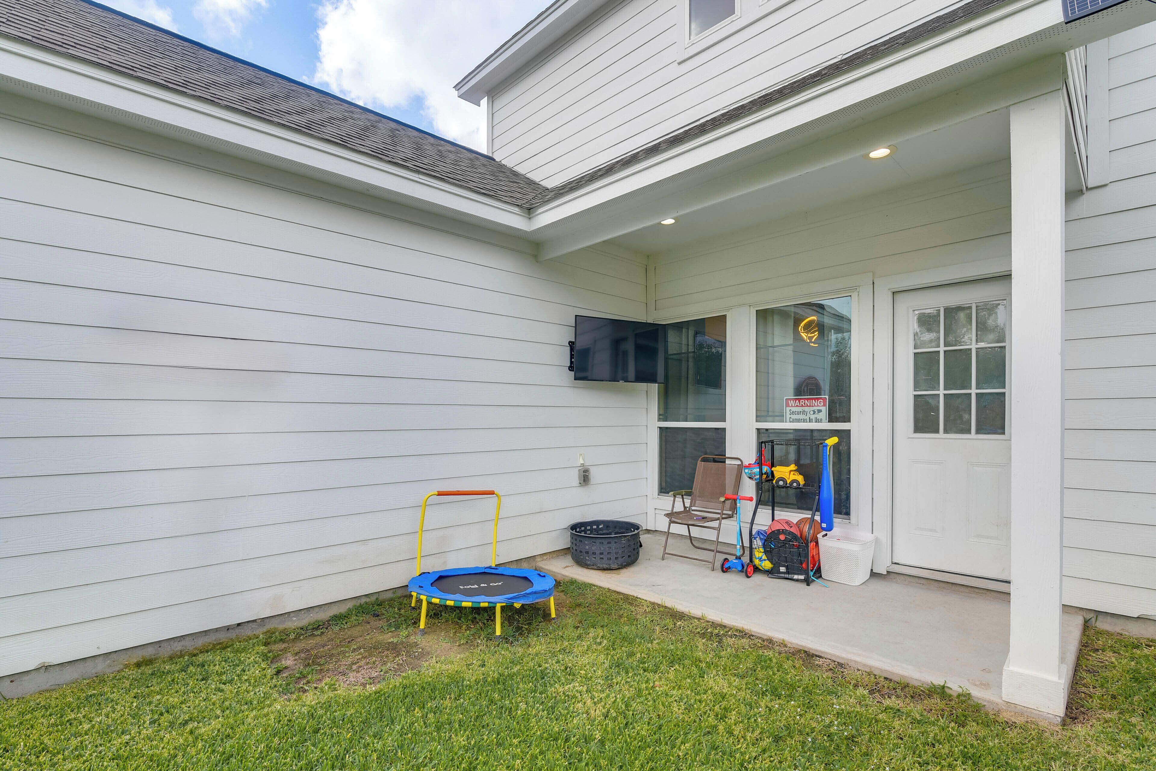 A residential exterior with a white house, a trampoline, a covered porch, and a security warning sign.