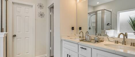 Une salle de bain moderne avec un grand miroir, deux lavabos et un espace douche.
