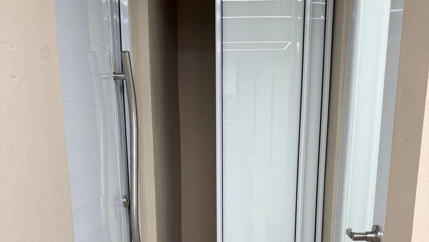 En smal gang med en skydedør, der fører til et rum. Gulvet er flisebelagt, og væggen er beige.