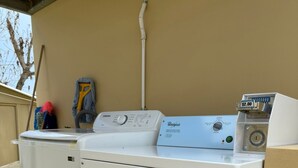A front-loading Whirlpool washer and dryer in a laundry room with a beige wall, a mop, and cleaning supplies. - Caleno Boricua apartment. Modern luxury apartment 5 minutes from the beach (Quebradillas)