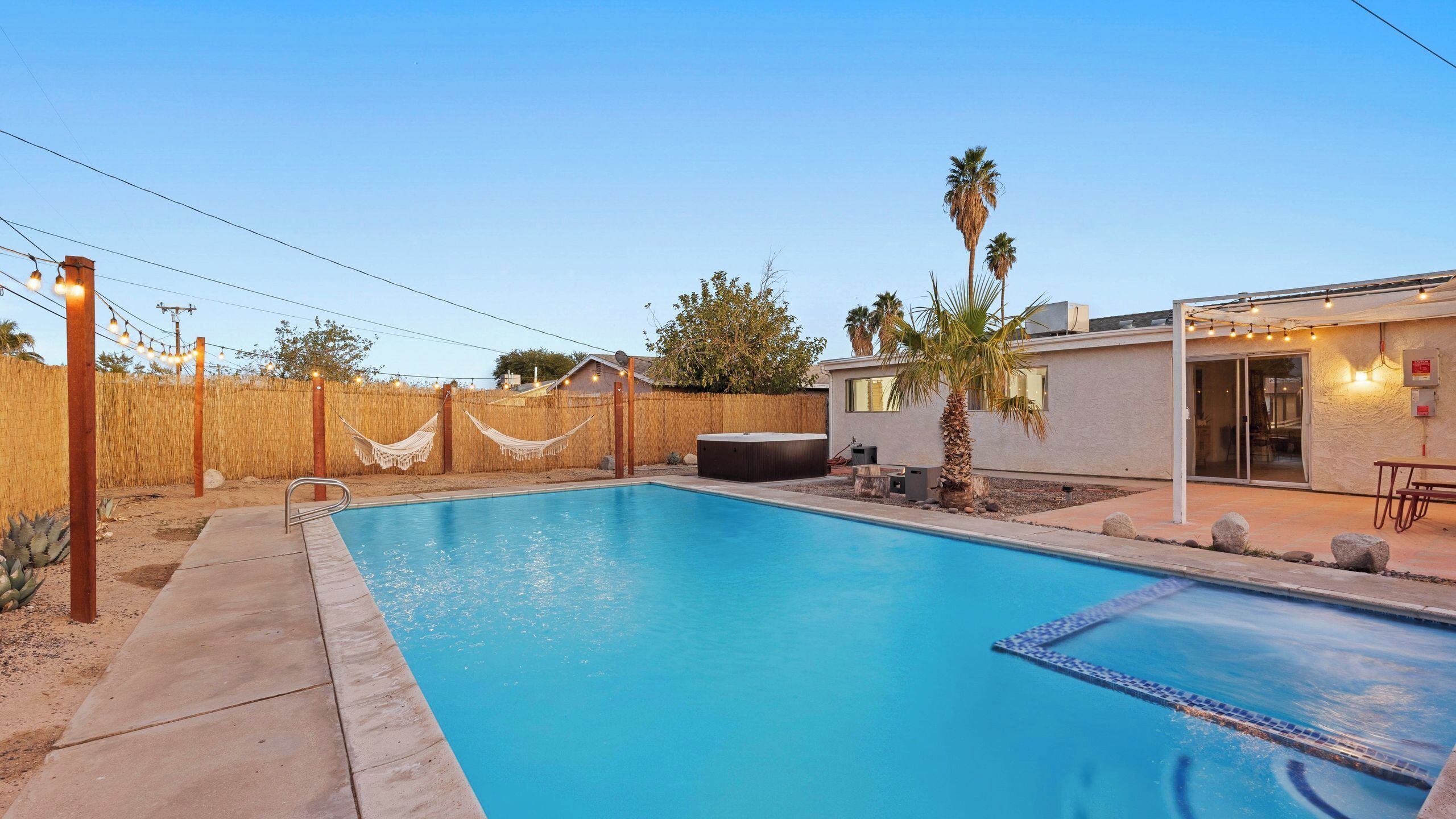Una piscina con jacuzzi, un patio cubierto y un patio cercado con una hamaca.