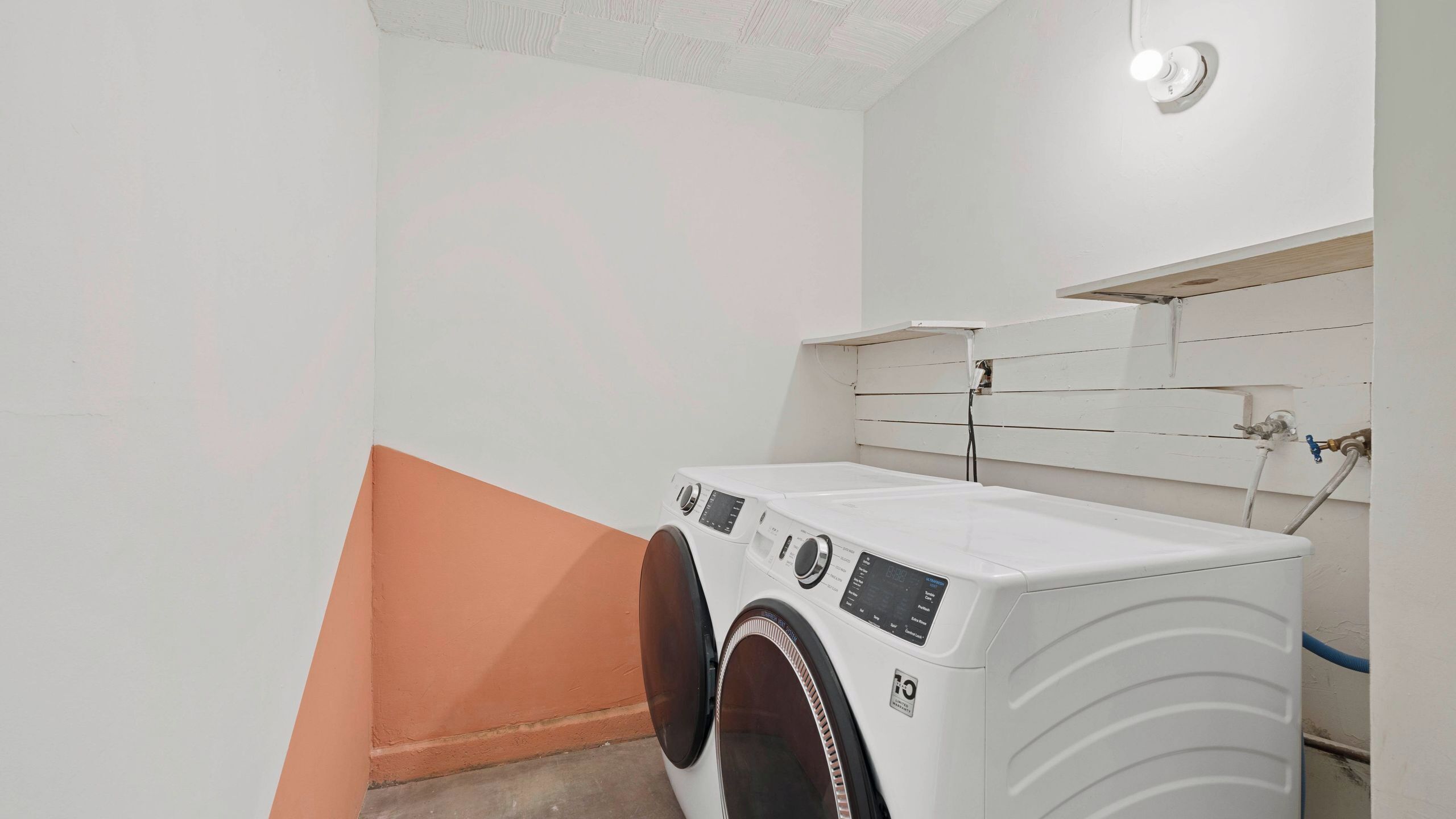 A laundry room with two front-loading washing machines, a white tiled wall, and a visible plumbing setup.