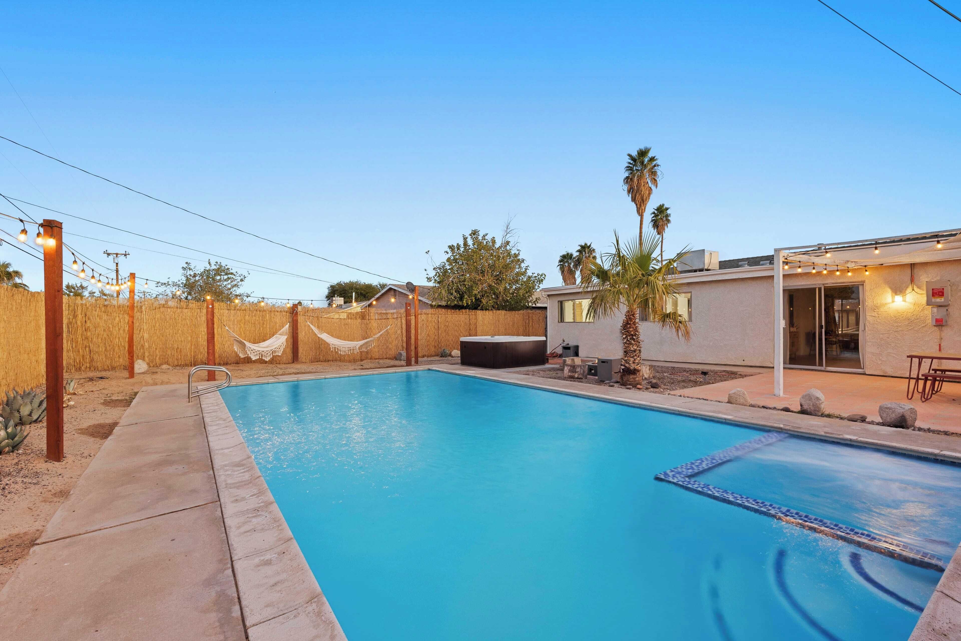 A swimming pool with a wooden fence, a hammock, and a small building with outdoor seating.
