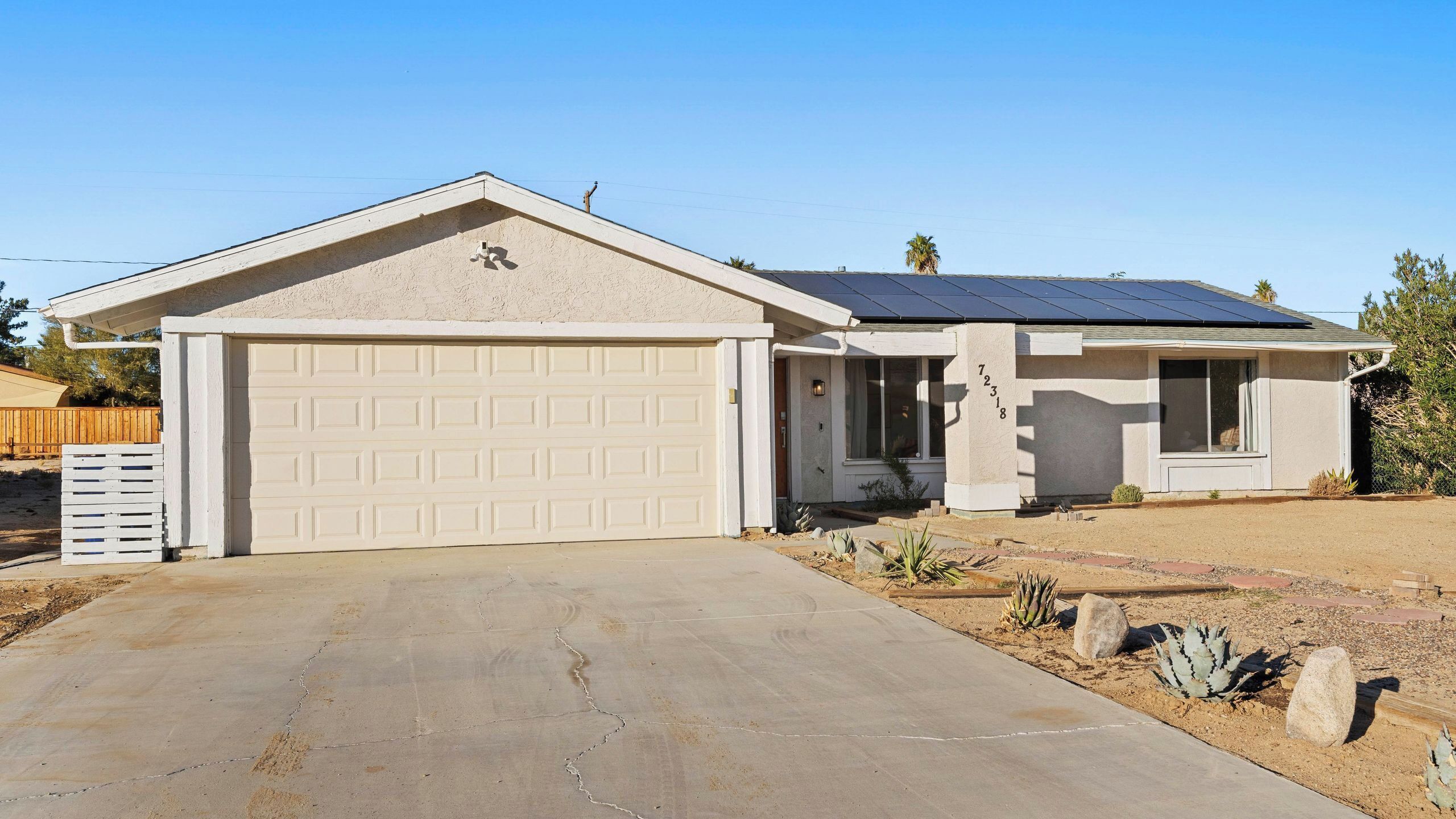A single-story house with a garage, a solar panel roof, and a desert landscape.