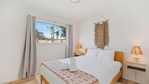 A bedroom with a bed, two bedside tables, a window with curtains, and a wall hanging.