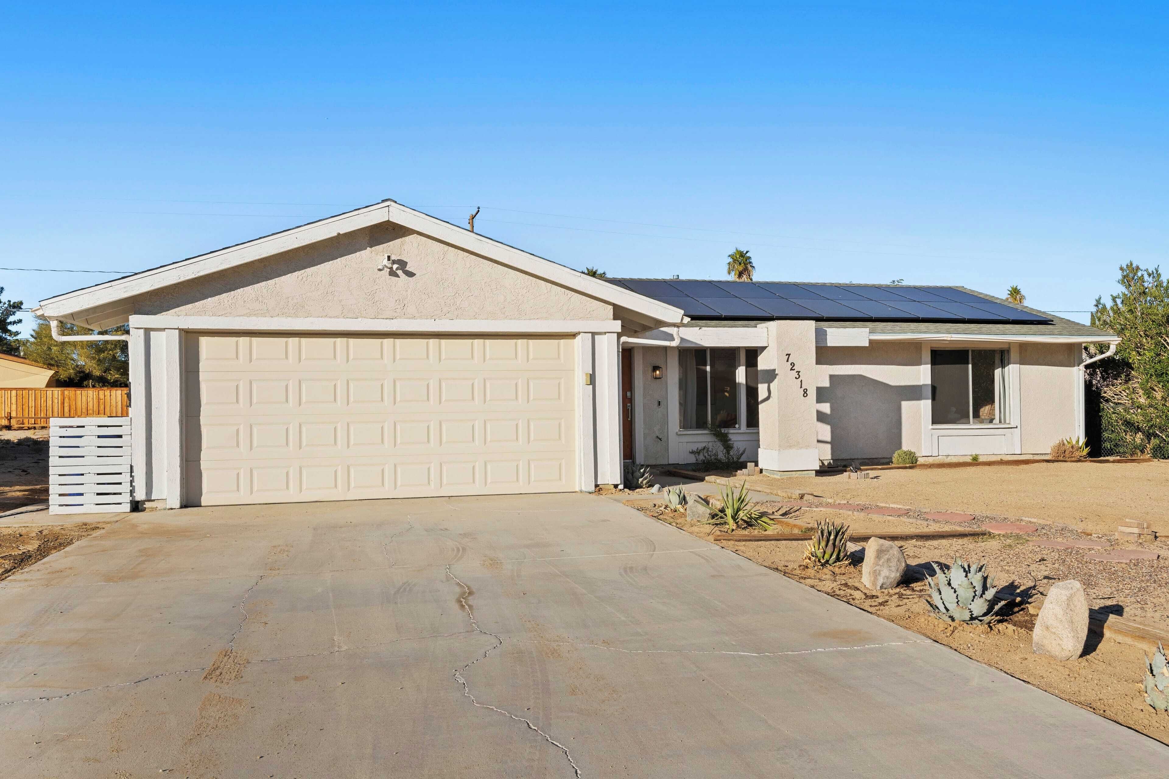 A single-story house with a garage, solar panels on the roof, and a desert garden.