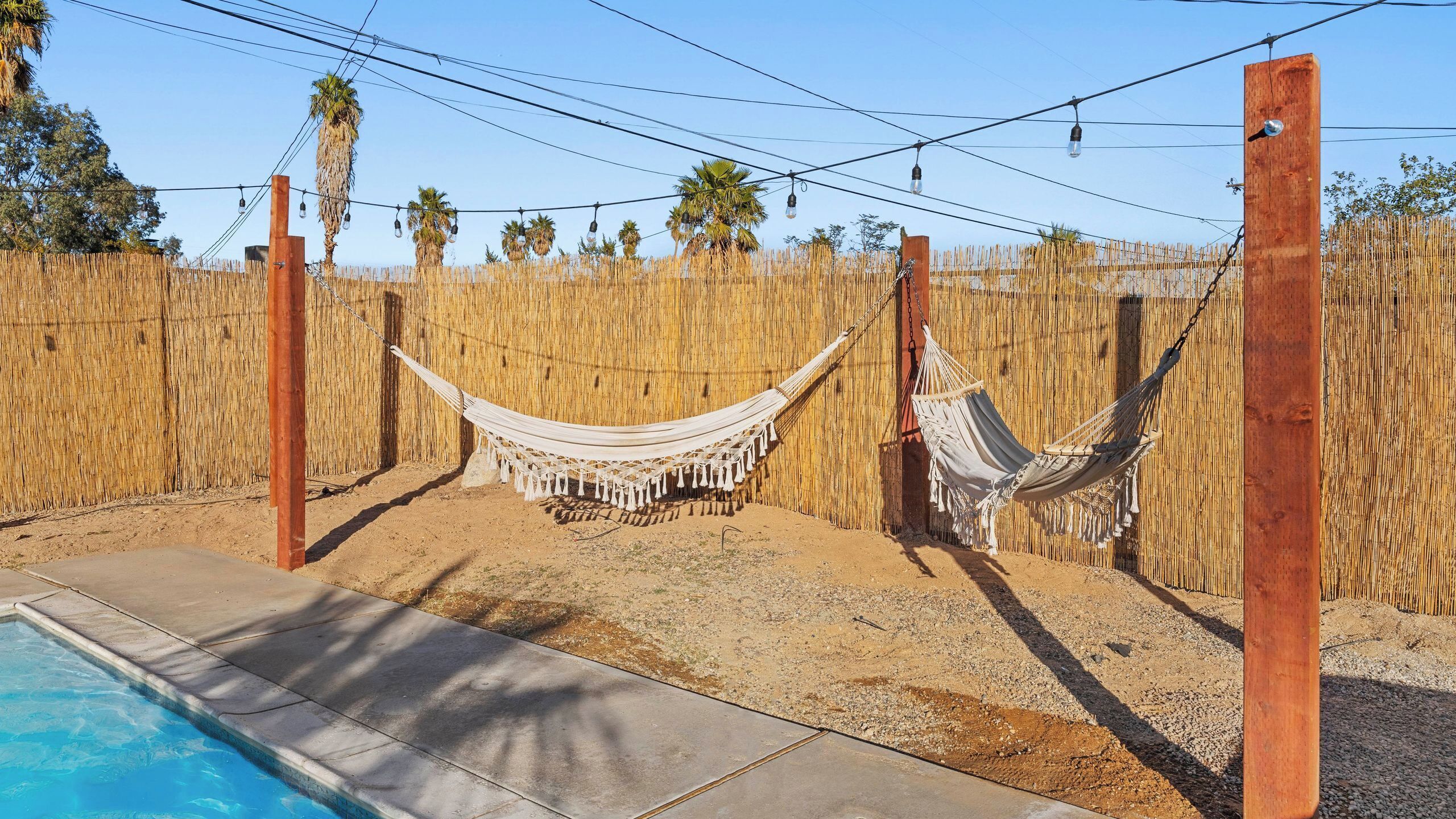 A hammock set up between two wooden posts, a pool, and a bamboo fence.