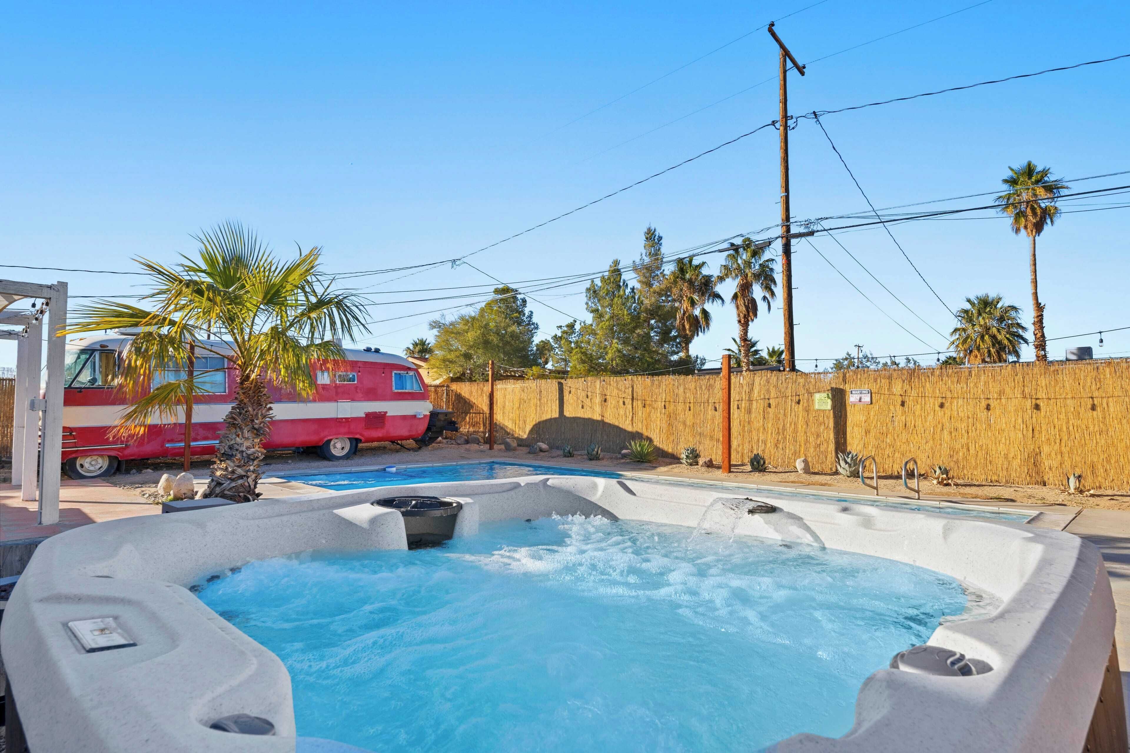 A hot tub area with a pool, palm trees, and a red vehicle in the background.