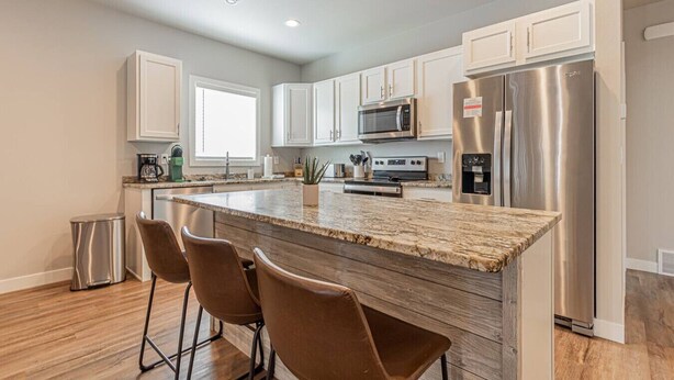 A modern kitchen with white cabinets, stainless steel appliances, a granite countertop, and a bar area with stools. - Cozy 3bd/2ba House in Horace (Horace)