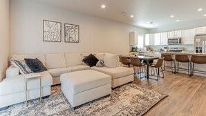 A modern living room with a sectional sofa, a dining area with a small table and chairs, and a kitchen with white cabinets and stainless steel appliances. - Cozy 3bd/2ba House in Horace (Horace)