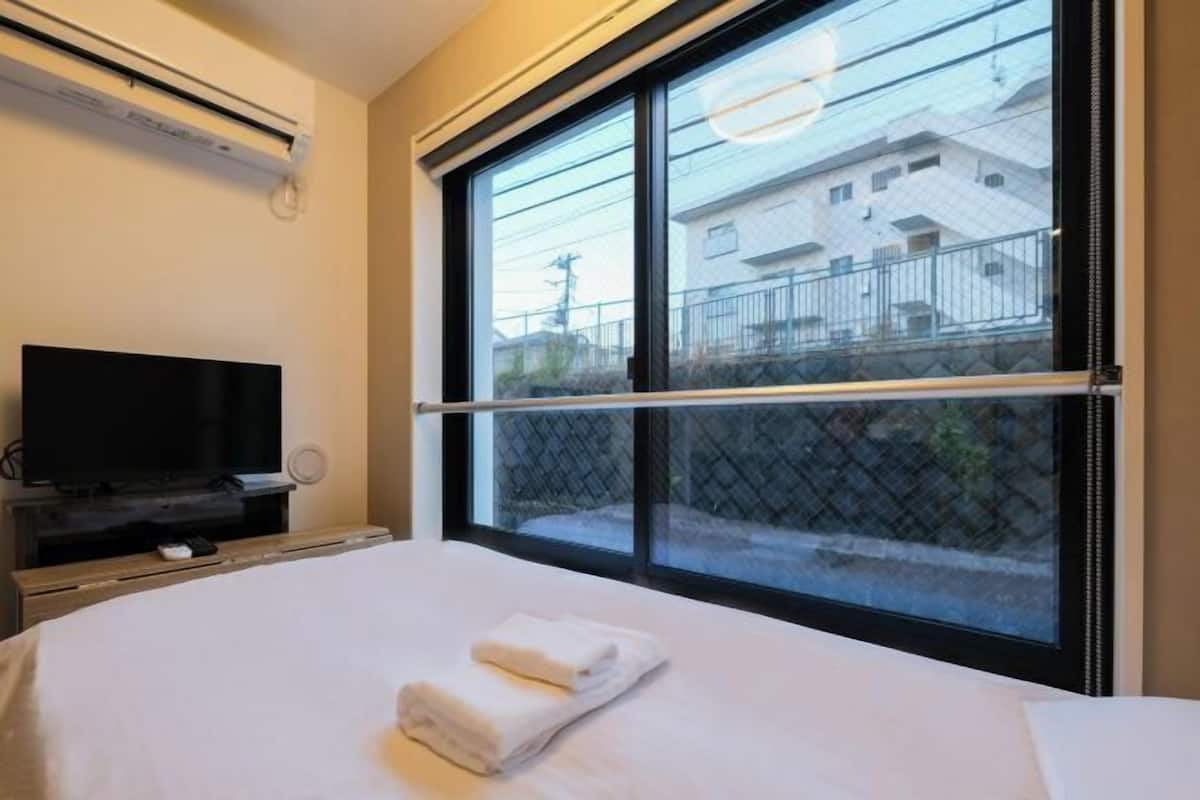 A hotel room with a bed, a TV, and a large window with a view of buildings.