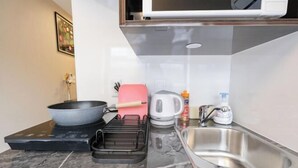 A modern kitchen with a built-in microwave, a kettle, a sink, and a stovetop with a pan and a griddle. - Mi-Hotel Qualia Shinjuku (Tokyo)