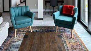 Un soggiorno moderno con due poltrone color petrolio, un tavolino in legno e un tappeto colorato.
