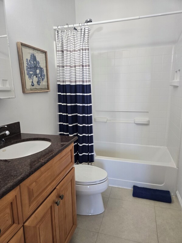 A bathroom with a white bathtub, a white toilet, a wooden vanity with a sink, and a striped shower curtain.