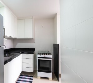 Eine kleine Küche mit integriertem Kühlschrank, einem Herd und weißen Schränken.