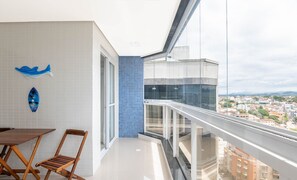 A balcony with a city view, a dining area with a table and chairs, and decorative wall art. - Apart With 2 Bedrooms 400 m From the Beach Ina1306 (Guarapari)