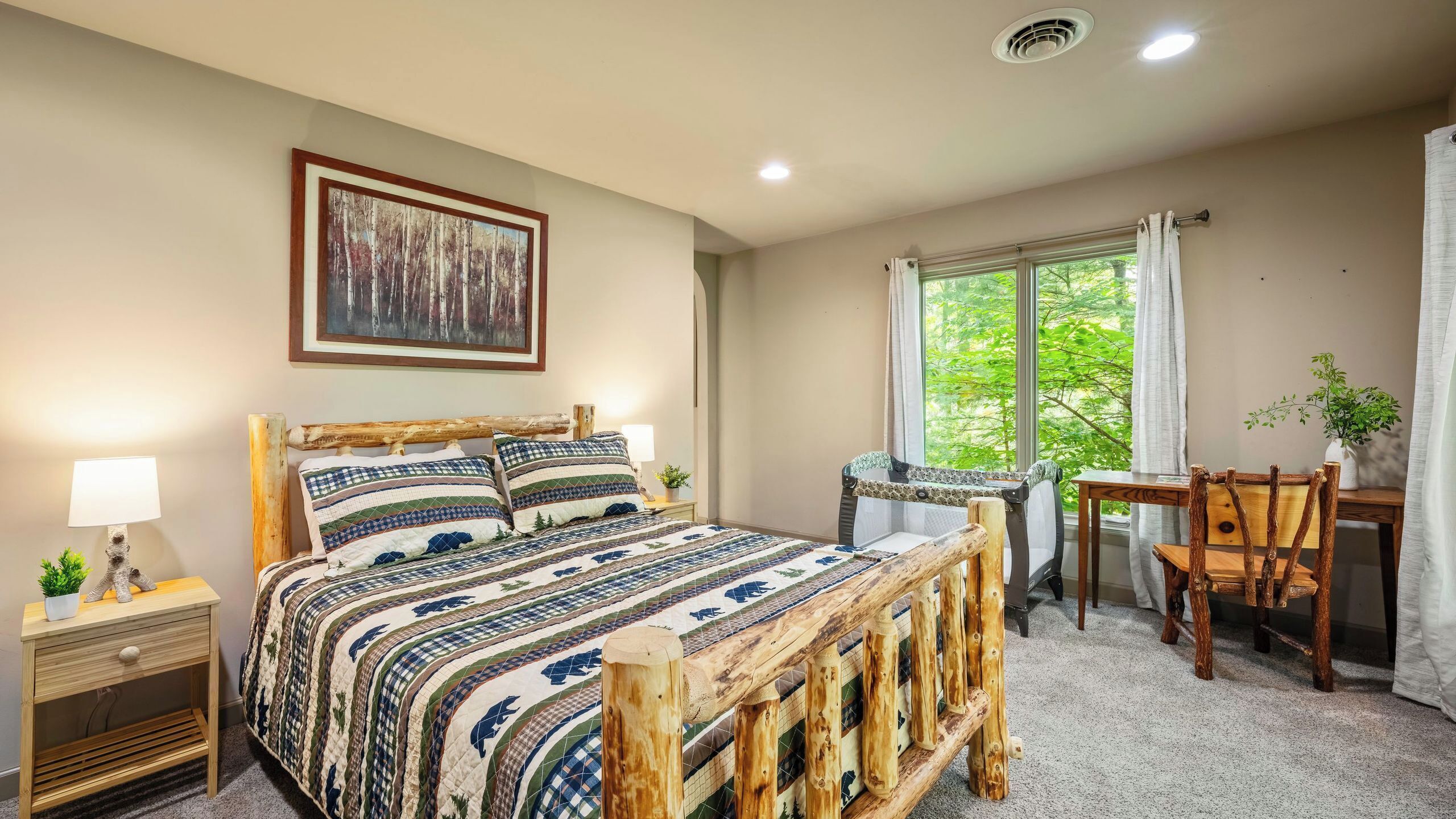 A bedroom with a bed, bedside tables, a chair, a table, a window with curtains, and a painting on the wall.