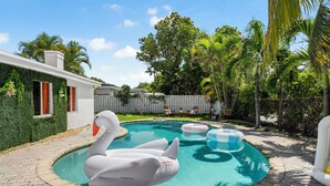 Piscina com boias de cisne inflável e aro, rodeada por um calçadão pavimentado e vegetação exuberante.