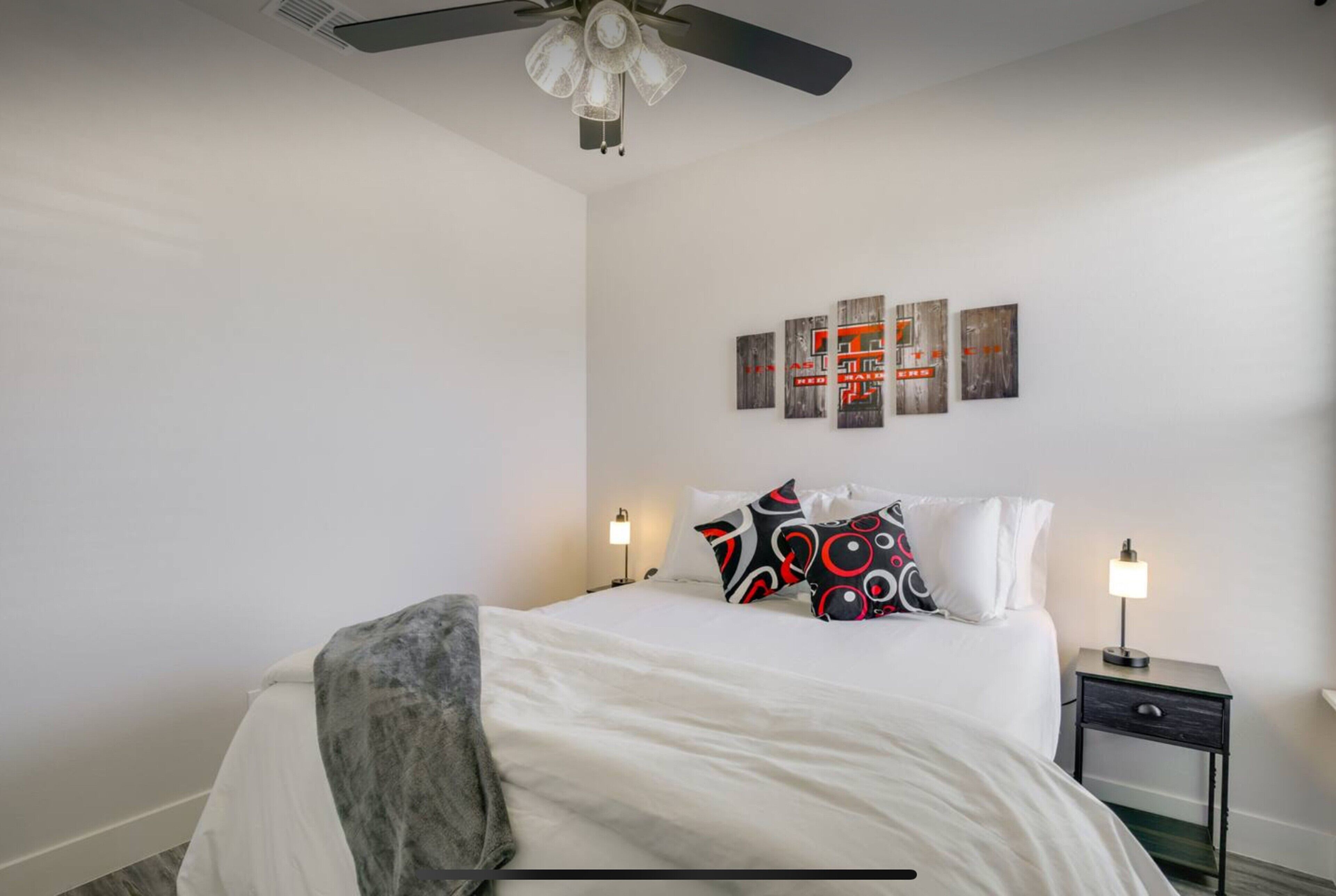 A neatly arranged bedroom with a bed, two bedside tables with lamps, a ceiling fan, and wall art.