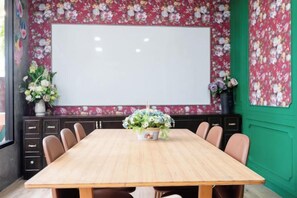 Ein Konferenzraum mit großem Tisch, Stühlen, einer Whiteboard-Tafel und blumigem Wandpapier.