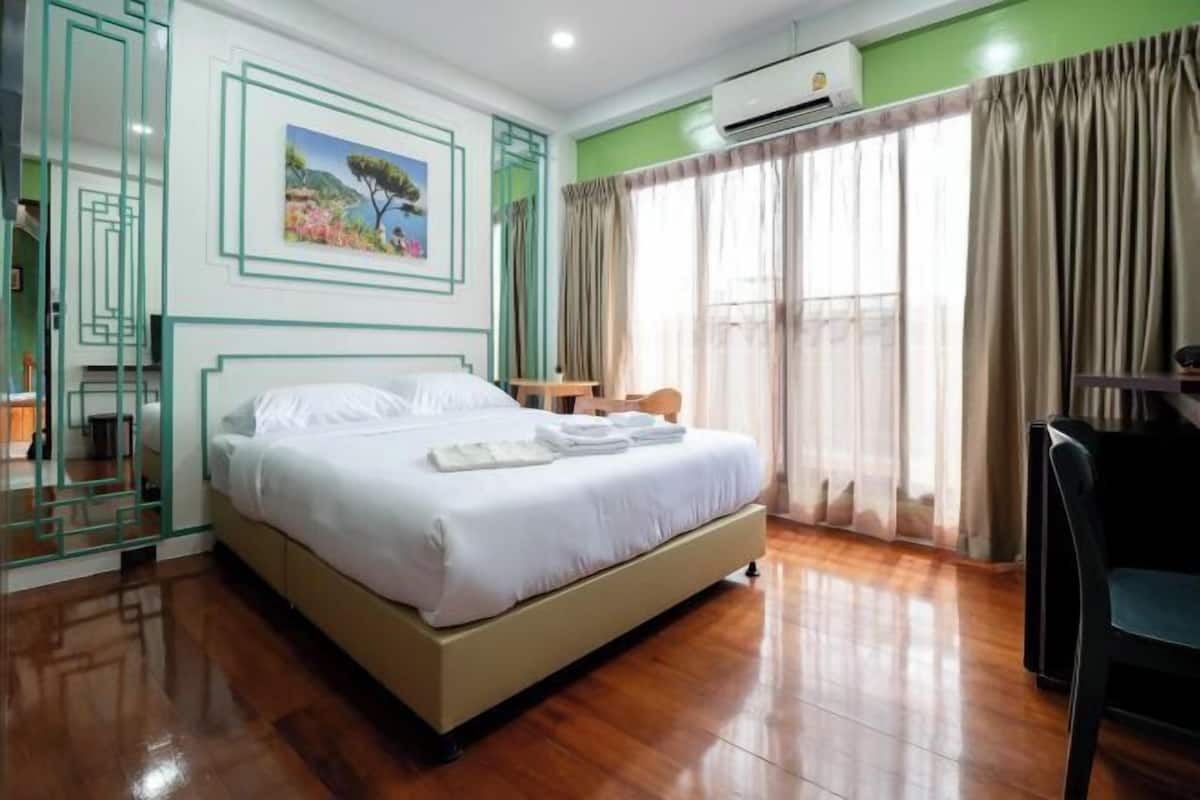 Une chambre d’hôtel avec un lit, un bureau, une chaise, une fenêtre avec des rideaux et un tableau au mur.