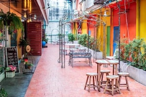 Un café en plein air avec des tables et des chaises, entouré de plantes en pot et bordé d’un chemin en briques.