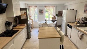 A modern kitchen with white cabinets, a central island, and a dining area with a table and chairs. - Large house with swimming pool - sleeps 13, sleeps 25 - near Paris (rebais)