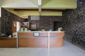 A reception desk with a stone wall backdrop, a wooden counter, and a framed notice. - New Panjang Jiwo Resort Syariah (Sukaraja)