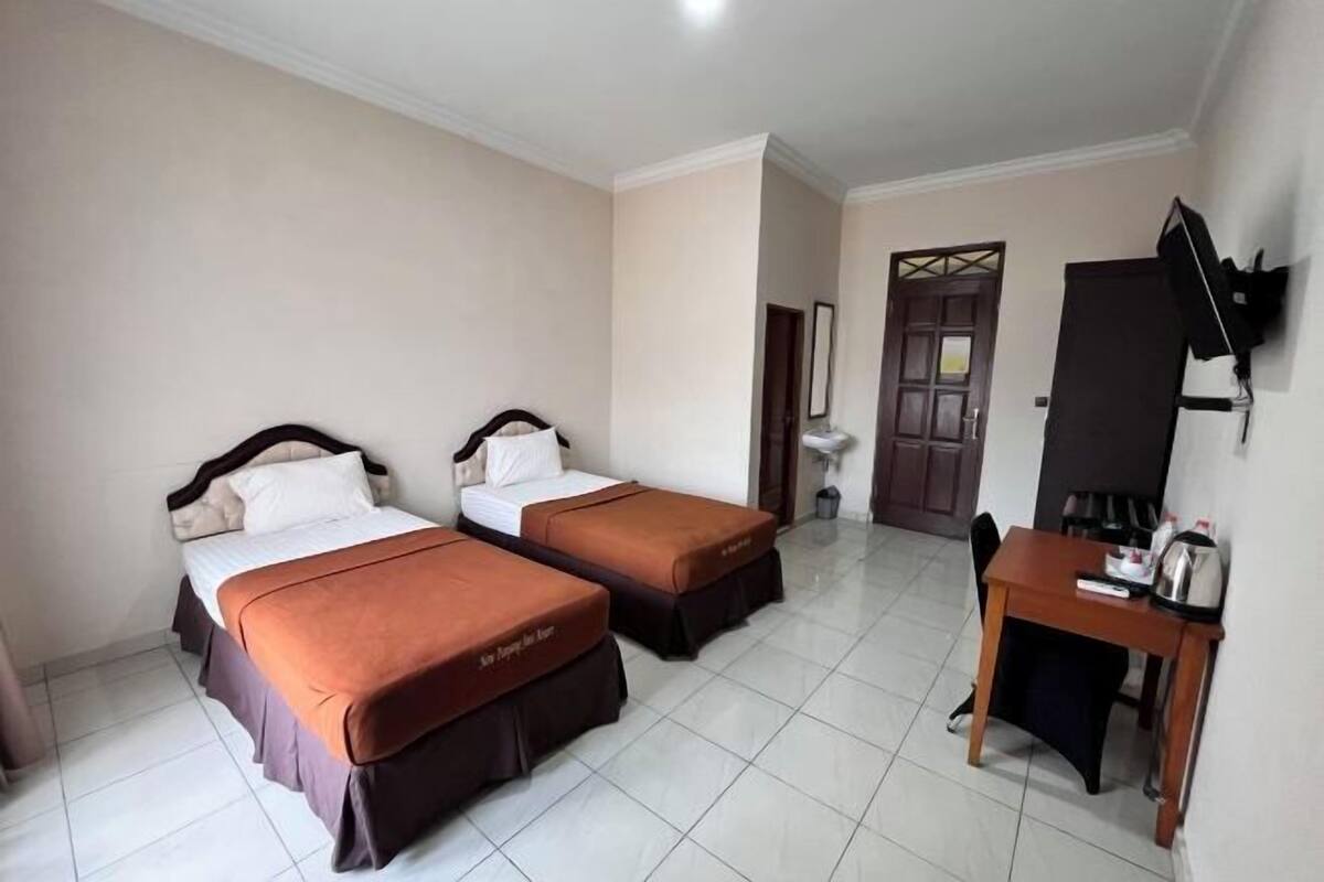 A hotel room with two beds, a desk, a chair, and a television mounted on the wall.