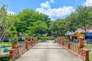 A bridge leading to a building with a tiled roof, surrounded by greenery and a body of water. - New Panjang Jiwo Resort Syariah (Sukaraja)