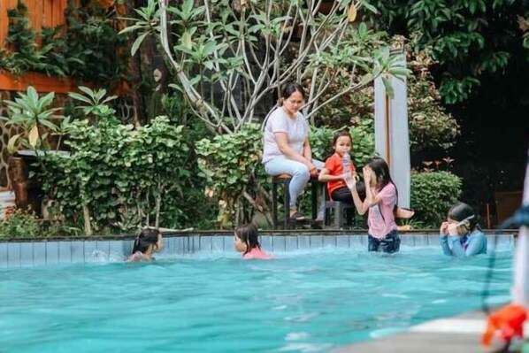 A swimming pool with people enjoying the water, surrounded by lush greenery. - New Panjang Jiwo Resort Syariah (Sukaraja)