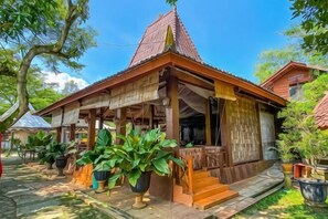 A traditional wooden structure with a tiled roof, surrounded by potted plants and a clear sky. - New Panjang Jiwo Resort Syariah (Sukaraja)