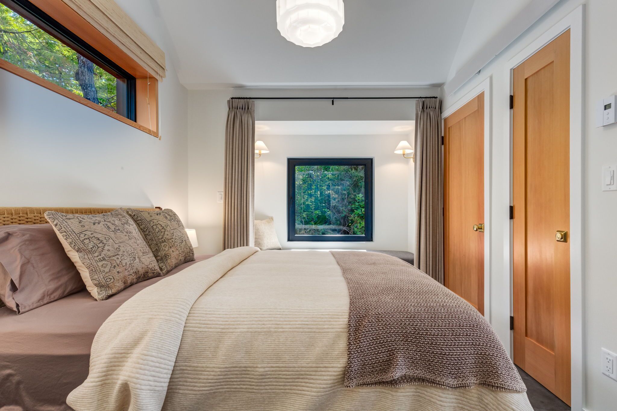 A bedroom with a large bed, a window with curtains, and a view of greenery.