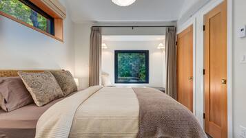 A bedroom with a large bed, a window with curtains, and a view of greenery.