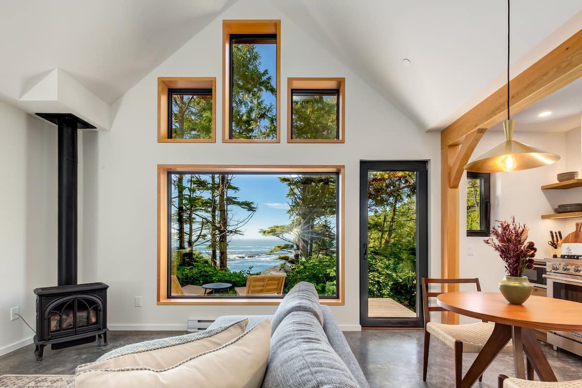 A modern living room with a large window overlooking a scenic ocean view, a cozy fireplace, and a dining area with a wooden table and chairs.